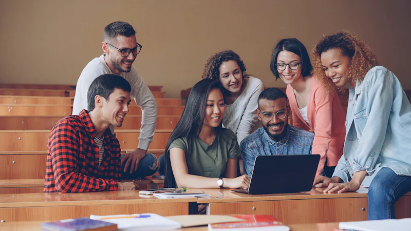 Un groupe d’étudiantes et d’étudiants souriants, réunis autour d’un ordinateur portable.