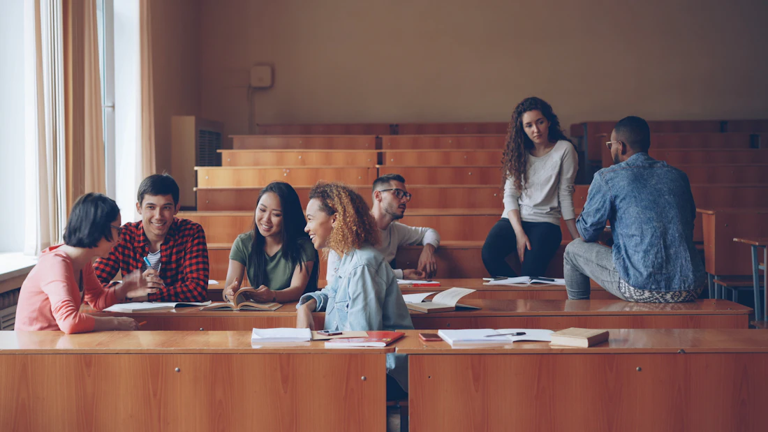 Un groupe mixte d’étudiantes et d’étudiants discute et rit entre deux cours, dans un amphithéâtre.
